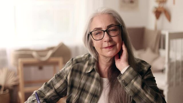 Inspired beautiful gray haired senior woman thinks questioningly imagine plan in mind has doubts create idea at desk at home workplace Happy smiling mature female with creative solution indoors