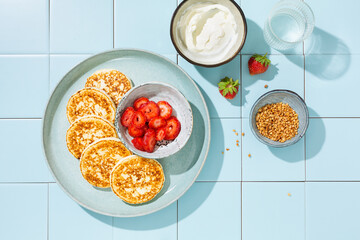 Homemade cheese pancakes with fresh strawberries, sour cream and grated nuts. Tile background. Hard light.