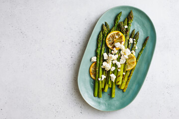 Grilled asparagus with soft cheese and lemon on a blue oval plate.