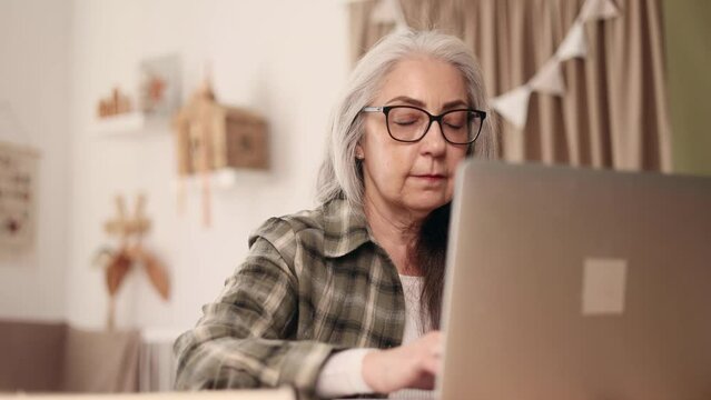 Close up portrait of senior woman with glasses relaxing at home or working online browsing products in internet store reading news checking email or social media profile on laptop computer indoors