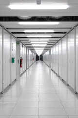 Long interior empty corridor hallway illuminated by neon lights with locker doors across both side, no people