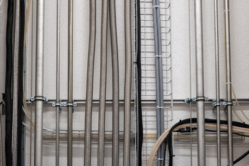 Vertical wall mounted pipes and electrical cables in an industrial setting. Front view, no people