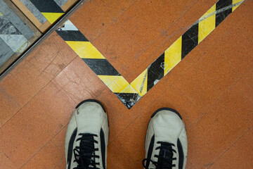 Male feet in shoes standing close to a no trespassing security tape on the floor of a building interior. Top view, unrecognizable person