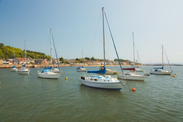 Fototapeta na wymiar Sailboats anchored in the Firth of Forth on a sunny summer day at the coastal seaside village of Limekilns, Fife, Scotland, UK.