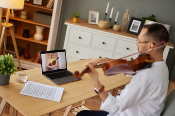 A female student learning from a music teacher to play the violin online using a laptop.
