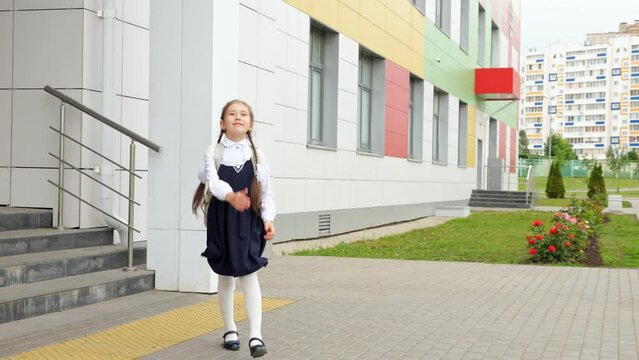 Junior schoolgirl leaves school with excited and happy expression skipping on stairs. Brown-haired girl in uniform walks jumping on way home