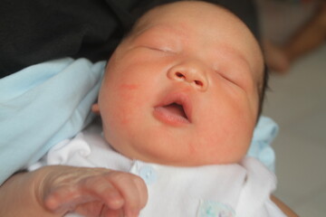 Portrait of a newborn boy who sleeps sweetly and smiles in he sleep in red clothes at a photo shoot of newborns
