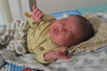 Portrait of a newborn boy who sleeps sweetly and smiles in he sleep in red clothes at a photo shoot of newborns
