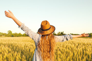 Fototapeta na wymiar Woman with long blond hair and a straw hat in a wheat field.