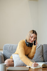 Asian female talking on the phone and writing a book with a smiling face, Working at home, Home lifestyle, Stay home.