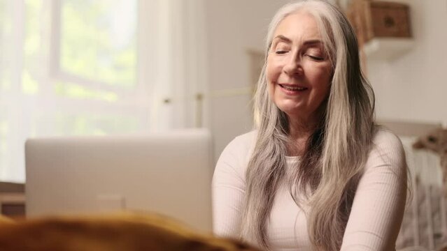 Portrait of beautiful gray haired senior woman having video call conference meeting interview by laptop computer at light home Smiling mature female talking on working or personal conversation indoors