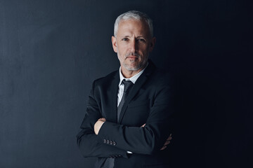 Senior executive, business man and arms crossed with confidence in portrait and management on dark background. Male CEO, corporate director and suit with ambition, empowerment and career in studio