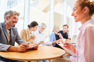Cheerful businessman and businesswoman discussing at table by colleagues sitting in office lounge