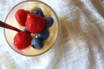 Glass of vanilla pudding, decorated with blueberries and starwberries. Served on the wooden table with beige tablecloth. Top view.