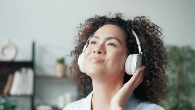 Video of beautiful young woman listening to music with headphones while dancing ans singing with smartphone in the living room at home.