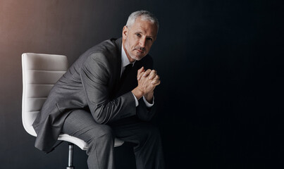 Portrait, manager or corporate with a business man sitting on a chair in studio against a dark background. Leadership, management and a senior male CEO in a professional suit for his executive career - Powered by Adobe