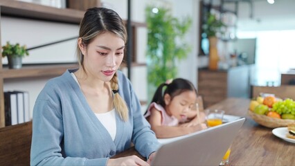 Young asian mother working on laptop while little daughter doing homework at home. Working and education concept, Single mother concept