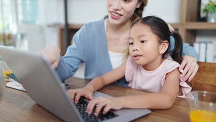 Fototapeta na wymiar Happy asian mother and little daughter using laptop for studying online or doing homework. Mother helping daughter using laptop. Online education, Technology concept