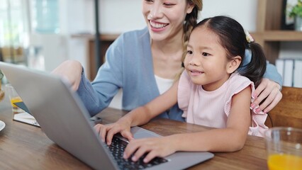 Fototapeta na wymiar Happy asian mother and little daughter using laptop for studying online or doing homework. Mother helping daughter using laptop. Online education, Technology concept