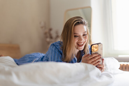 Young woman lying on a bed and scrolling her smartphone.