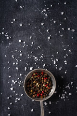 Big old spoon with peppercorn and salt pile on black background