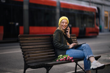 Young woman sitting in a city with flowers and digital tablet.