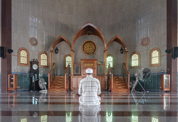 Religious muslim man sits and recite prayers for God on the floor in the Al Alawi Mosque. He prays...