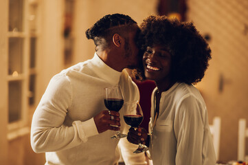 African american couple having romantic date at home while drinking wine and kissing - Powered by Adobe