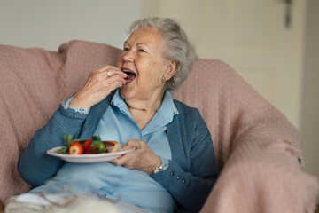 Senior woman resting at home and eating strawberries.
