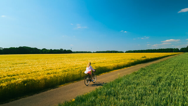 Aerial drone shot of young woman cyclist riding down beautiful countryside road between agricultural fields on sunny summer day. Healthy lifestyle