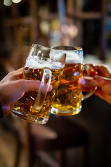 man and woman hands clinking with glasses of light beer at the pub or bar