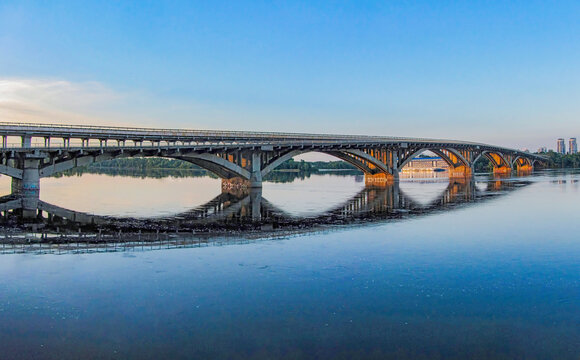Arch of the Metro bridge Brovary avenue over the Dnieper river in Kiev, Ukraine. In background the Pishokhidnyy Mist Cherez Dnipro Pedestrian bridge across the Dnieper