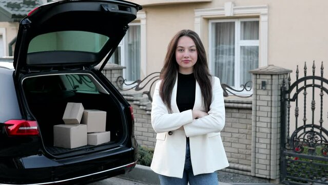 Young business woman standing at the car with parcels, coming home by car. The girl is standing and talking on mobile phone near the car