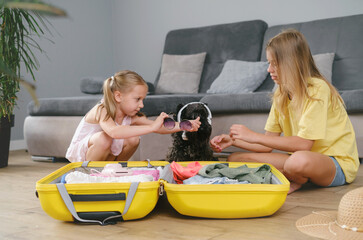 Children packing suitcase for travel and play with a dog. Sisters having fun with pet while getting ready for a trip. Dog in sunglasses and sunhat. going on vacation