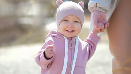 Excited toddler enjoys walking and holding mother hand at resort. Toddler girl with amused expression smiles and laugh during walking