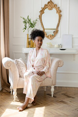 Young african woman in pajamas sitting in armchair and looking at camera.