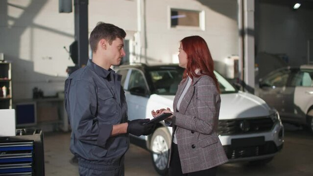 maintenance of a vehicle, a male mechanic with a tablet in his hands explains to frustrated woman owner of car about an engine breakdown at a technical station