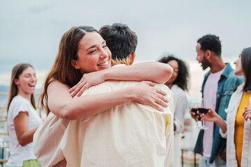 Happy young woman giving a hug to her boyfriend on a social festive party with their best friends. Affectionate couple embracing each other on a social gathering. Glad female greeting her husband