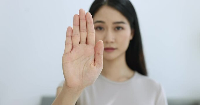Close up serious Asian woman show palm to camera demonstrate stop gesture, sign of anti domestic violence, racism racial discrimination, fight for women rights, pose indoor look with strict expression