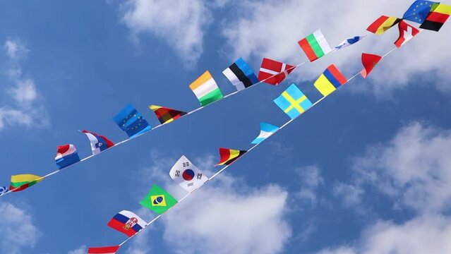 Flags of different countries flutter in the wind against a peaceful clear sky
