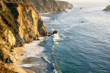 View of the rugged coast of central California from Bixby bridge at sunset in autumn. People enjoying the magnificent view are visible at the foot the steep cliff.
