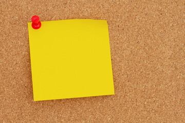 Blank yellow sticky note with a pushpin on a corkboard