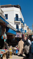 Alley lined with souvenir shops below white buildings with blue trim in the Medina in Essaouira, Morocco