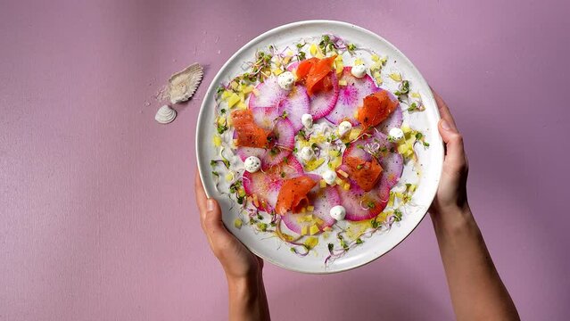 plate with a fancy fish dish on a pink tabel with water shadows, woman holding the plate