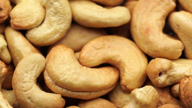 Cashew Pieces on a turntable from overhead. Plant based ingredient. Dried cashew nuts. Macro shot. Raw snack. Pile cashew nuts without shell, rotates, close up. Whole nut kernels. Rotation