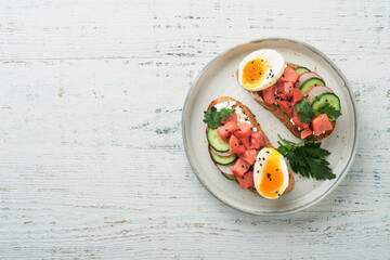 Healthy sandwich with bread or toast, smoked salmon, soft egg, cream cheese, cucumber, radish, black sesame and parsley on old wooden table. Delicious protein fish sandwich for breakfast. Smorrebrod.