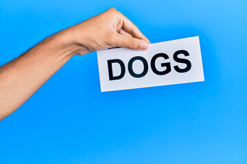 Hand of caucasian man holding paper with dogs word over isolated blue background