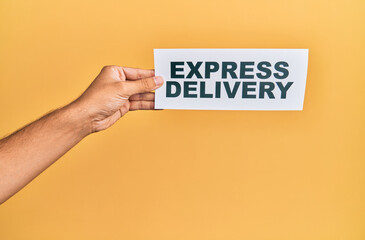 Hand of caucasian man holding paper with delivery express message over isolated yellow background