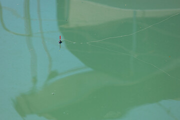 Fishing float with line on the water surface. Blurred shadows on the water