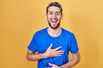 Hispanic man with beard standing over yellow background smiling and laughing hard out loud because funny crazy joke with hands on body.